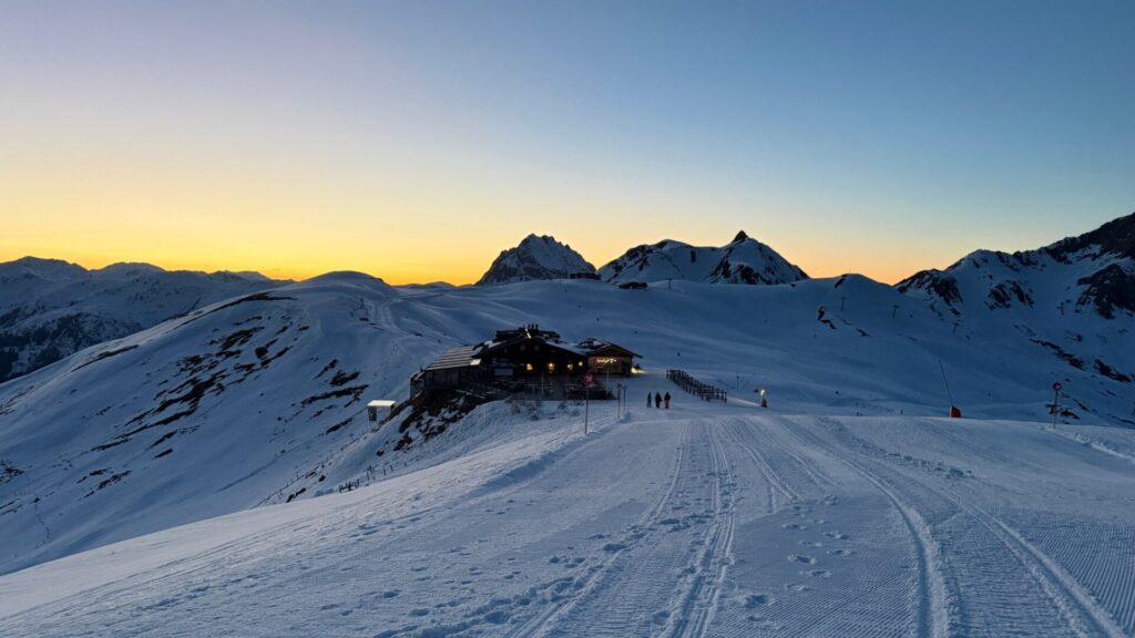Verlichte berghut aan de piste bij zonsondergang